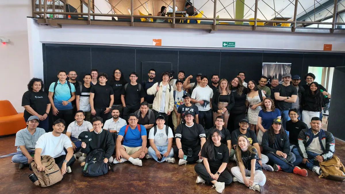 Grupo grande reunido en un salón de dos niveles, con gente sentada en el piso.