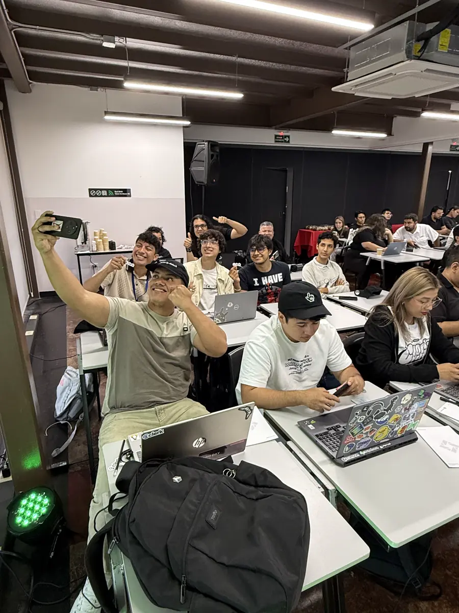Salón de clases: una persona se toma una selfie y otras usan laptops en las mesas.