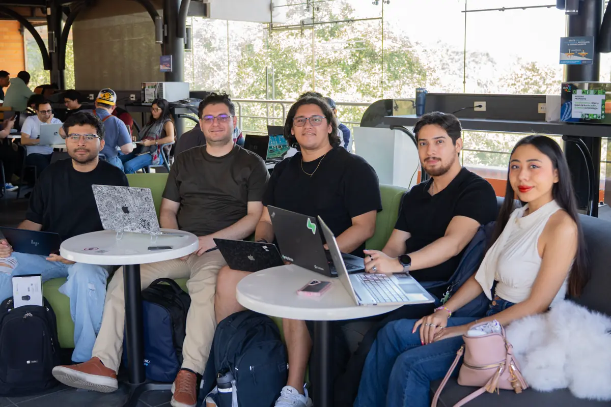 Cinco personas en un sofá verde, con laptops abiertas sobre mesas redondas.