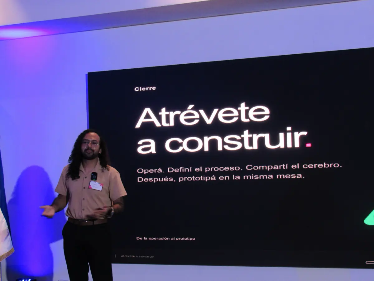 Una persona de pie junto a una pantalla negra que dice “Atrévete a construir”.